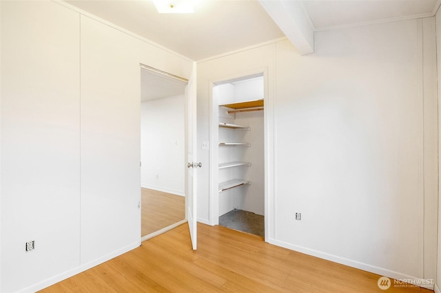 unfurnished bedroom with baseboards, beam ceiling, crown molding, and light wood finished floors