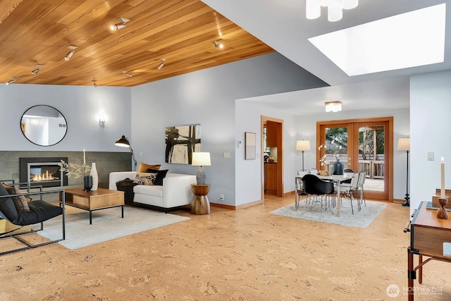 living area featuring a glass covered fireplace, wooden ceiling, french doors, and baseboards