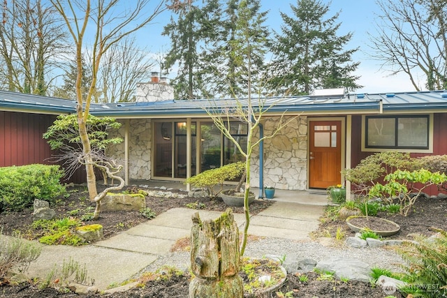 view of front of home featuring a standing seam roof, metal roof, stone siding, and a chimney