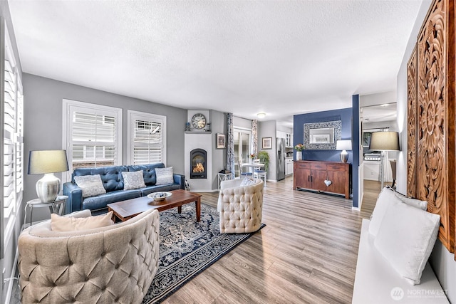 living area featuring a textured ceiling, a glass covered fireplace, and light wood finished floors