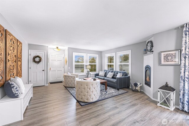 living room with light wood-type flooring, baseboards, and a warm lit fireplace