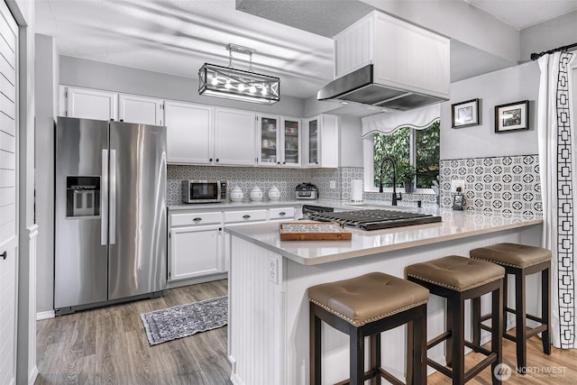 kitchen featuring backsplash, glass insert cabinets, a peninsula, light wood-style floors, and stainless steel appliances