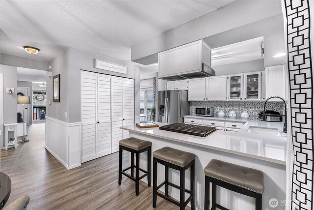 kitchen with a sink, wood finished floors, appliances with stainless steel finishes, a peninsula, and white cabinets