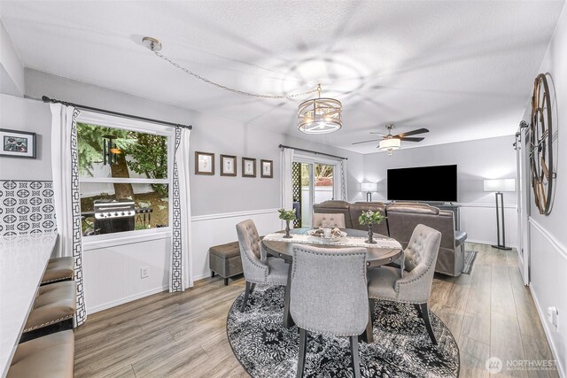 dining area with baseboards, a textured ceiling, light wood-style flooring, and ceiling fan with notable chandelier