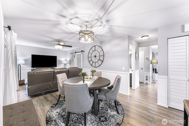 dining room with ceiling fan, a barn door, a textured ceiling, and light wood-style flooring