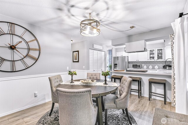 dining room with a chandelier, a wainscoted wall, and light wood-style floors