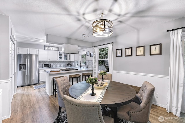 dining area featuring light wood finished floors, a chandelier, wainscoting, and a textured ceiling