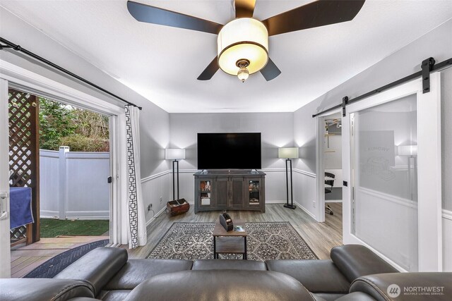 living room with a barn door, wood finished floors, a ceiling fan, and baseboards