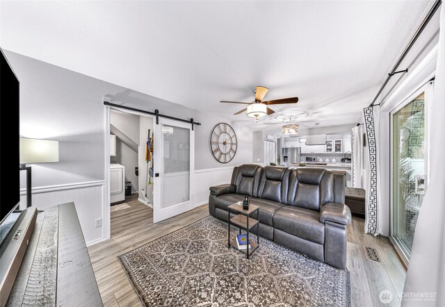 living area with a barn door, visible vents, a ceiling fan, and light wood finished floors