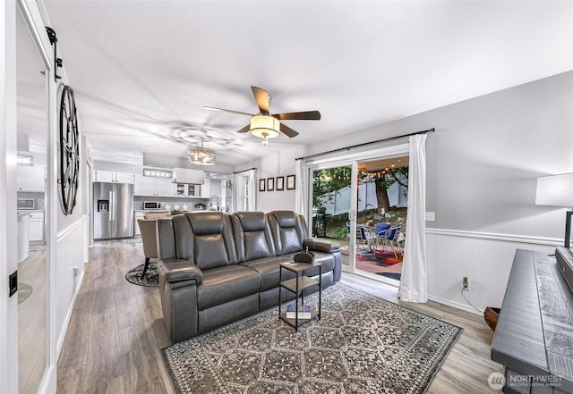 living area with light wood finished floors, a wainscoted wall, ceiling fan, and a barn door