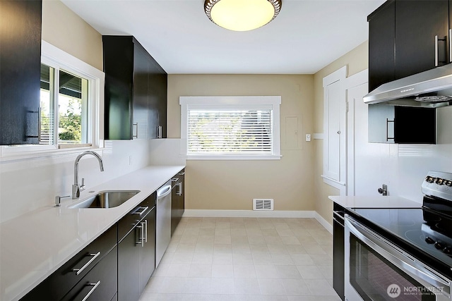 kitchen featuring visible vents, range hood, dark cabinetry, stainless steel appliances, and a sink