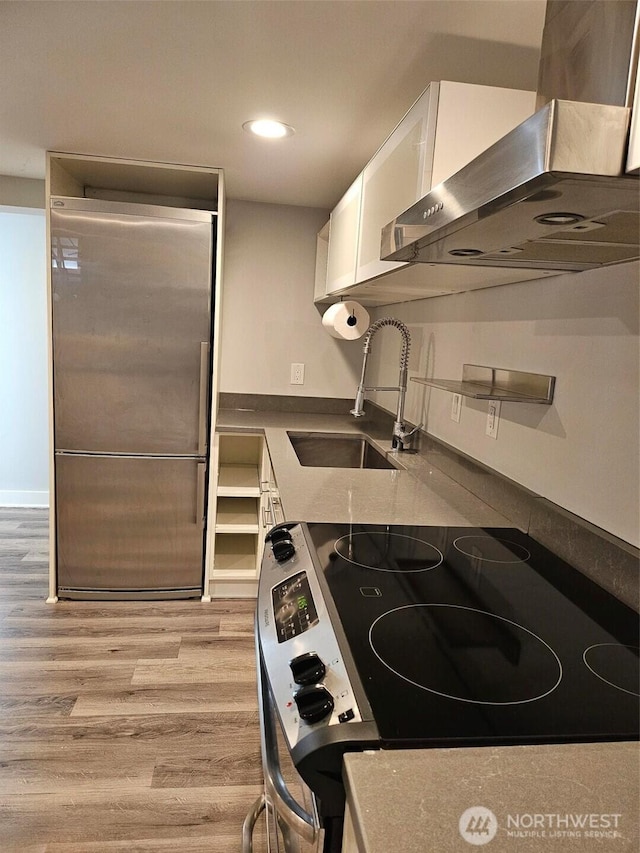 kitchen featuring range with electric stovetop, exhaust hood, stainless steel fridge, white cabinetry, and a sink