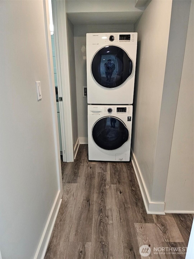 clothes washing area with laundry area, wood finished floors, baseboards, and stacked washing maching and dryer