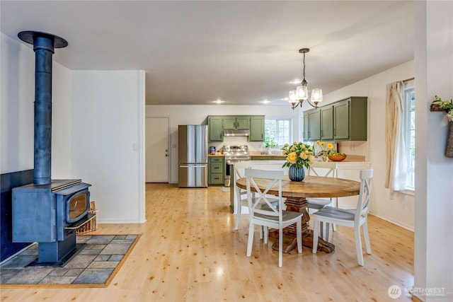 dining room featuring a notable chandelier, light wood-type flooring, a wood stove, and baseboards