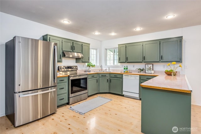 kitchen featuring green cabinets, under cabinet range hood, appliances with stainless steel finishes, a peninsula, and a sink