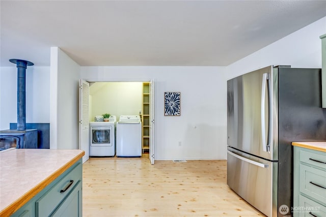 kitchen featuring washing machine and dryer, light wood-type flooring, light countertops, freestanding refrigerator, and a wood stove