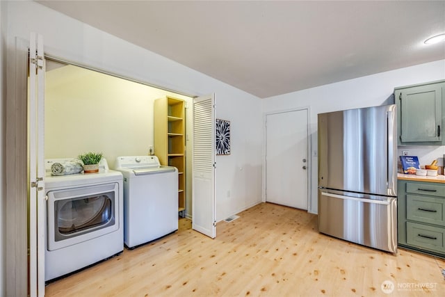 clothes washing area with laundry area, baseboards, light wood finished floors, and washing machine and clothes dryer