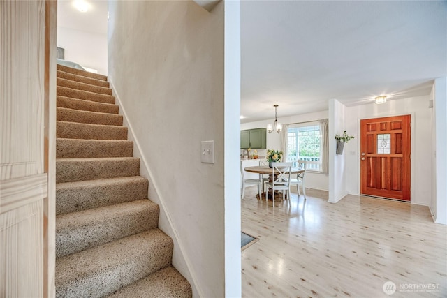 staircase with a notable chandelier, wood finished floors, and baseboards