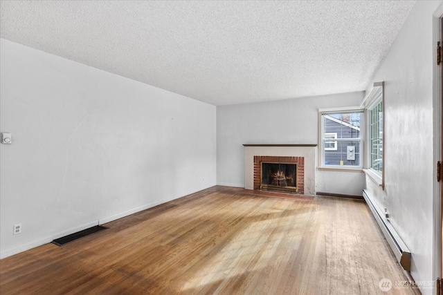 unfurnished living room featuring a baseboard radiator, a brick fireplace, visible vents, and wood finished floors