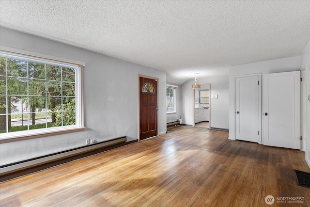 unfurnished living room featuring a textured ceiling, wood finished floors, visible vents, and a baseboard radiator