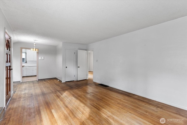 unfurnished living room featuring a textured ceiling, light wood-type flooring, and baseboards