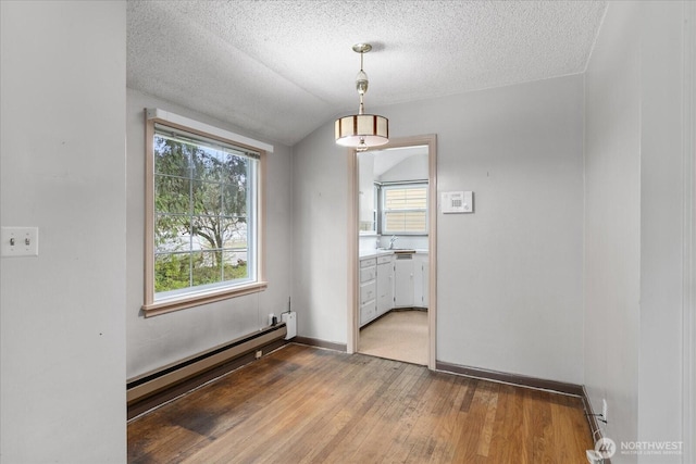 unfurnished dining area featuring plenty of natural light, light wood-style flooring, a baseboard heating unit, and vaulted ceiling