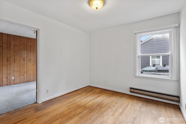 empty room featuring wooden walls, wood finished floors, baseboards, and a baseboard radiator