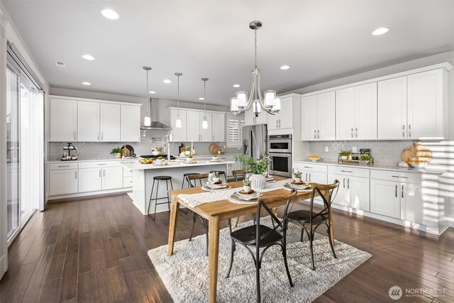 kitchen featuring a breakfast bar, stainless steel appliances, light countertops, dark wood-type flooring, and wall chimney exhaust hood