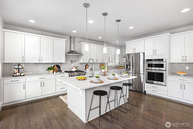 kitchen featuring wall chimney range hood, dark wood-style floors, appliances with stainless steel finishes, white cabinets, and light countertops