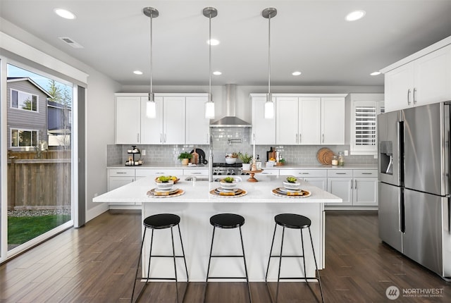 kitchen with a breakfast bar area, dark wood finished floors, light countertops, stainless steel refrigerator with ice dispenser, and wall chimney range hood