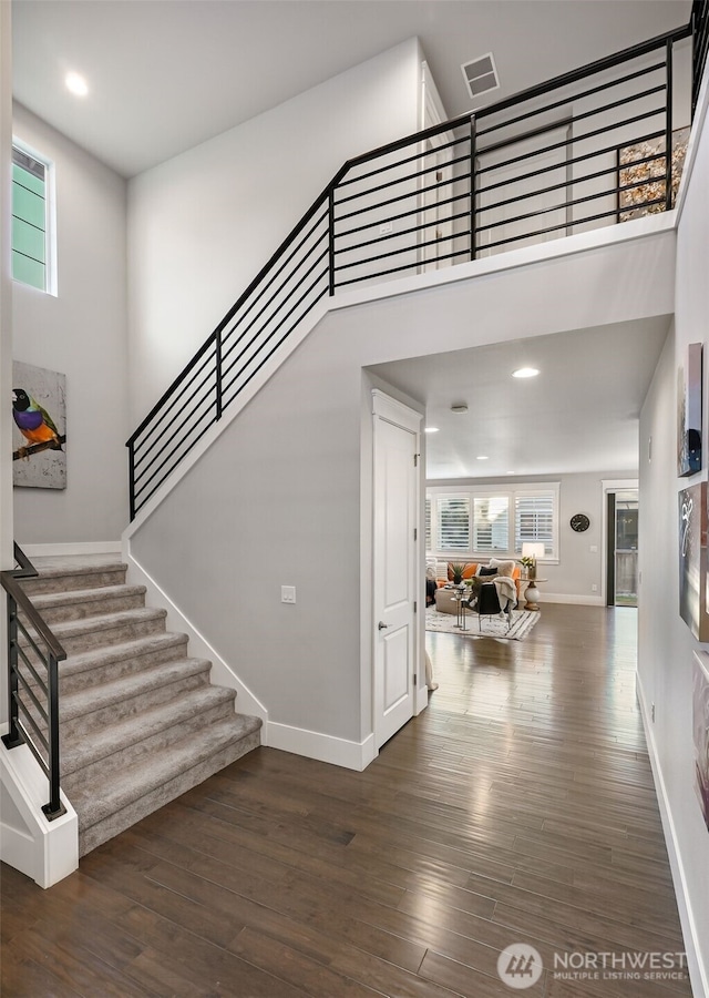 interior space featuring visible vents, stairs, a towering ceiling, and wood finished floors