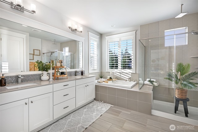 full bathroom featuring a bath, a shower stall, double vanity, and a sink