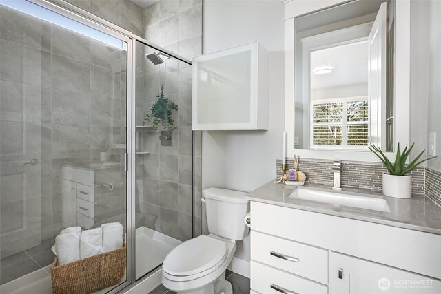 full bathroom featuring backsplash, a stall shower, vanity, and toilet