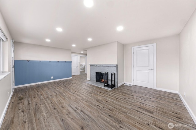 unfurnished living room with recessed lighting, a wainscoted wall, a multi sided fireplace, and wood finished floors