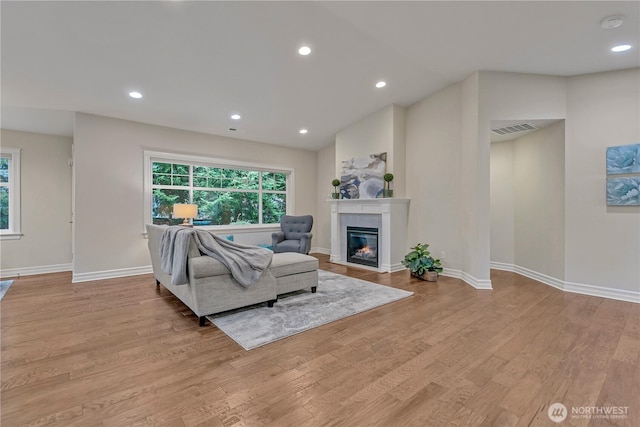 living area with wood finished floors, visible vents, baseboards, recessed lighting, and a glass covered fireplace