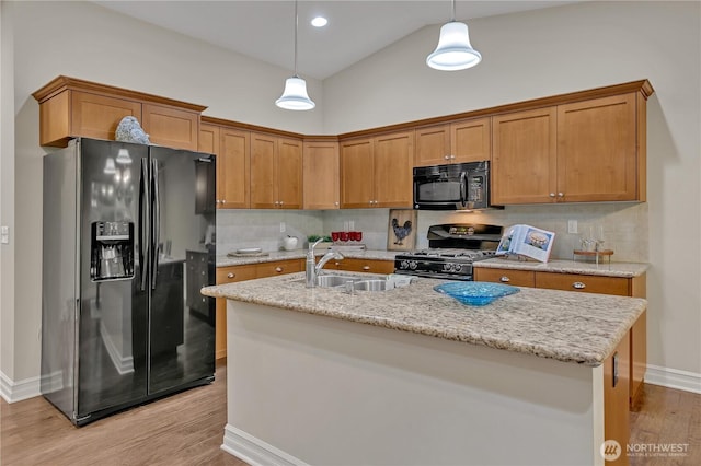 kitchen with decorative light fixtures, black appliances, light wood-type flooring, and a sink