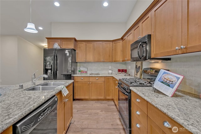 kitchen featuring black appliances, a sink, light stone counters, tasteful backsplash, and light wood-style floors