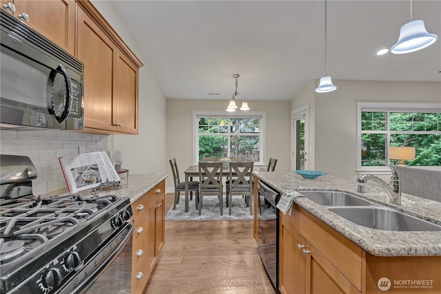 kitchen with light wood-style flooring, a sink, decorative backsplash, black appliances, and decorative light fixtures