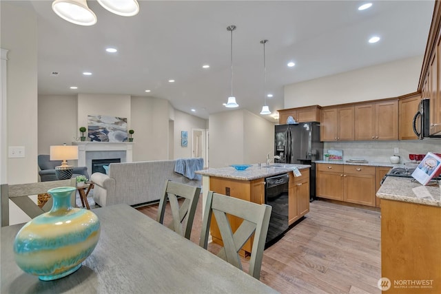 kitchen featuring light wood-type flooring, black appliances, light stone counters, a glass covered fireplace, and open floor plan