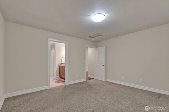 unfurnished bedroom featuring baseboards, light carpet, attic access, and ensuite bathroom