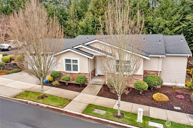 ranch-style home featuring concrete driveway, stone siding, and roof with shingles