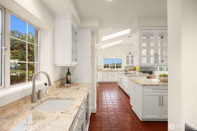 kitchen with dark tile patterned floors, a sink, white cabinets, glass insert cabinets, and light stone countertops