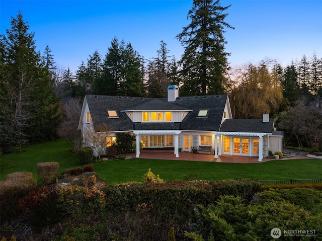 back of house at dusk featuring a patio, a lawn, french doors, and a chimney