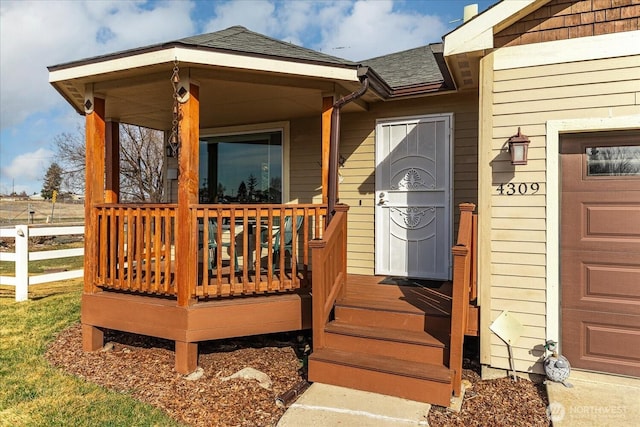 property entrance featuring an attached garage, covered porch, and a shingled roof