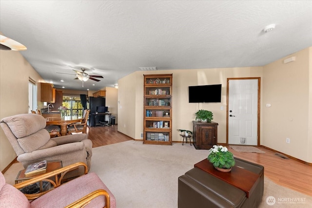 living area featuring baseboards, visible vents, a textured ceiling, and ceiling fan