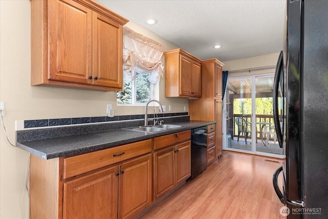 kitchen with light wood finished floors, a sink, black appliances, dark countertops, and brown cabinets