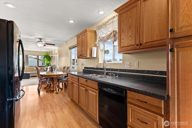 kitchen featuring black appliances, a sink, dark countertops, light wood-style floors, and brown cabinetry