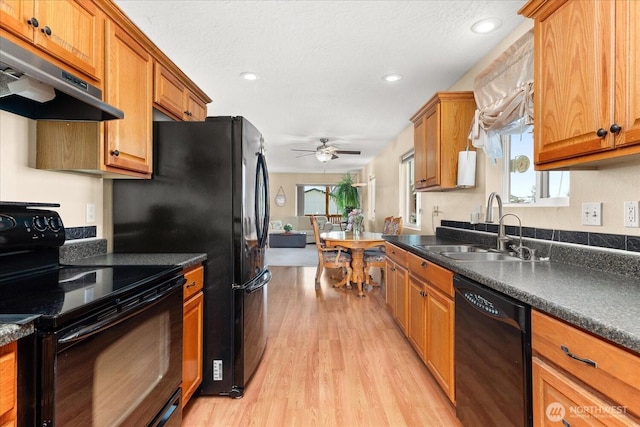 kitchen with brown cabinets, black appliances, under cabinet range hood, a sink, and dark countertops