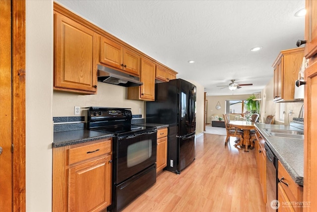 kitchen with brown cabinets, black appliances, under cabinet range hood, dark countertops, and light wood finished floors