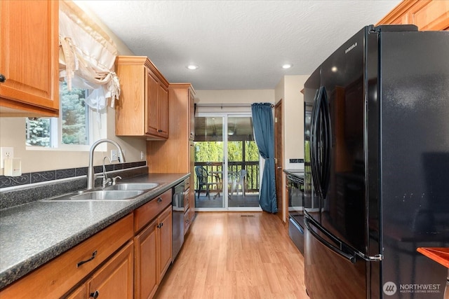 kitchen with black appliances, a sink, dark countertops, brown cabinetry, and light wood finished floors